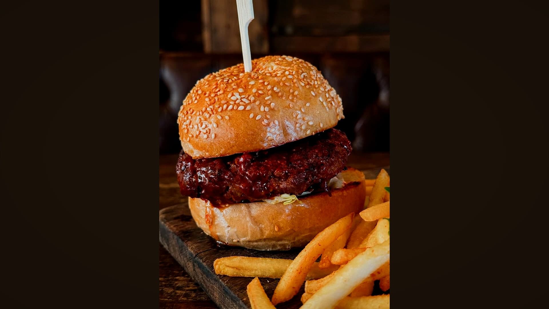 Aufgebauter Burger mit dickem Patty und Sesambrötchen, daneben Pommes — KI-generiertes Symbolbild