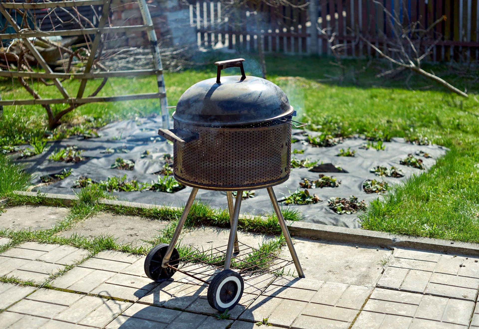 Kugelgrill im Garten, Rauch steigt aus dem geschlossenen Deckel